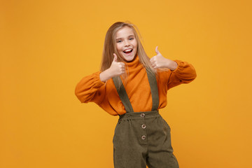 Funny little blonde kid girl 12-13 years old in turtleneck, jumpsuit isolated on orange yellow background children studio portrait. Childhood lifestyle concept. Mock up copy space. Showing thumbs up.