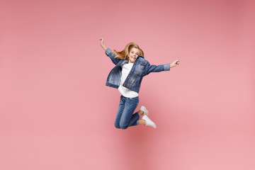 Smiling little blonde kid girl 12-13 years old in denim jacket isolated on pastel pink background children studio portrait. Childhood lifestyle concept. Mock up copy space. Jumping, spreading hands.