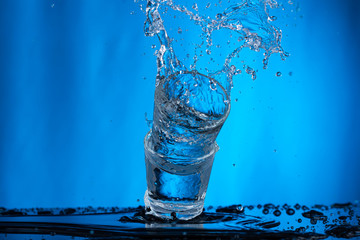 Fototapeta na wymiar Falling glasses of water on a blue background, vodka spills and a splash