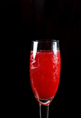 Red cocktail with champagne and fruit syrup in a champagne glass against the black background