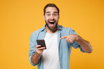 Excited young man in casual blue shirt posing isolated on yellow orange wall background studio...