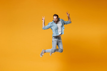 Fototapeta na wymiar Funny young bearded man in casual blue shirt posing isolated on yellow orange background studio portrait. People sincere emotions lifestyle concept. Mock up copy space. Jumping showing victory sign.