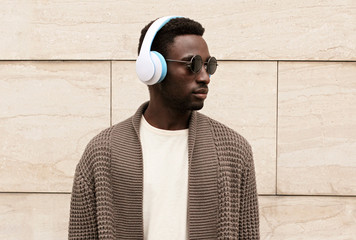 Portrait stylish african man in wireless headphones listening to music wearing brown knitted...