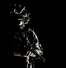 Army special operations forces soldier in mask and combat uniform, helmet equipped night-vision device, armed submachine gun with silencer, looking aside, low key studio portrait on black, copyspace