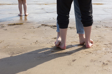 Woman feet standing on man feet and child feet on the sand beach barefoot