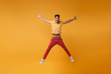 Fototapeta na wymiar Funny young african american guy in bright casual clothes posing isolated on yellow orange background studio portrait. People lifestyle concept. Mock up copy space. Jumping spreading hands and legs.