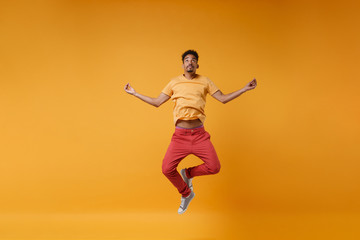 Young african american guy in bright casual clothes posing isolated on yellow orange background. People lifestyle concept. Mock up copy space. Jumping hold hands in yoga gesture, relaxing meditating.