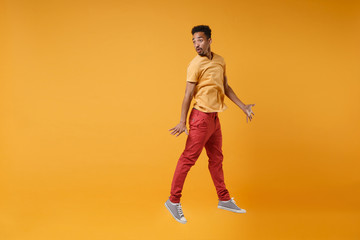 Fototapeta na wymiar Shocked young african american guy in casual clothes posing isolated on yellow orange background studio portrait. People lifestyle concept. Mock up copy space. Jumping spreading hands looking aside.