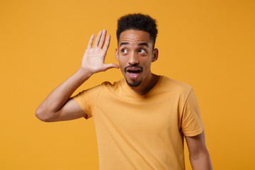 Curious young african american guy in casual t-shirt posing isolated on yellow orange wall...