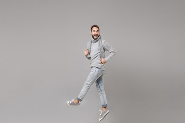 Fototapeta na wymiar Cheerful young bearded man in gray sweater scarf posing isolated on grey background studio portrait. Healthy fashion lifestyle people sincere emotions cold season concept. Mock up copy space. Jumping.