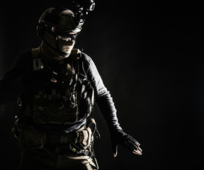 Naklejka premium Special operations fighter in helmet with night-vision, thermal imaging device, load carrier carefully moving with caution in darkness, holding hand on pistol, ready for fight during dangerous mission