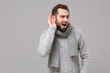 Curious young man in gray sweater, scarf posing isolated on grey wall background studio portrait....