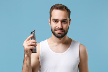 Close up bearded young man 20s years old in white shirt hold electric razor isolated on blue pastel...