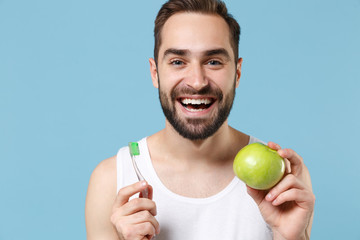 Bearded young man 20s years old in white shirt hold brush and green apple isolated on blue pastel...