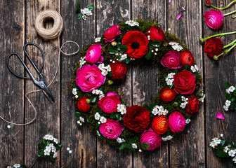 Handmade wreath with red, pink ranunculus flowers and white hawthorn blossom on old rustic background. Florist work concept. Top view.