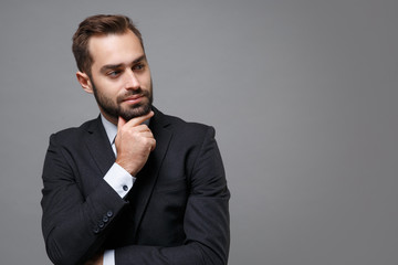 Pensive young business man in classic black suit shirt tie posing isolated on grey background....