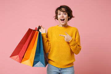 Excited young brunette woman girl in yellow sweater posing isolated on pink background. People lifestyle concept. Mock up copy space. Pointing indx finger on package bag with purchases after shopping.