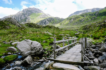 Wooden bridge and footpath crossing stream leading towards mountains