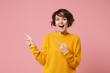 Cheerful young brunette woman girl in yellow sweater posing isolated on pastel pink background studio portrait. People sincere emotions lifestyle concept. Mock up copy space. Point index finger aside.