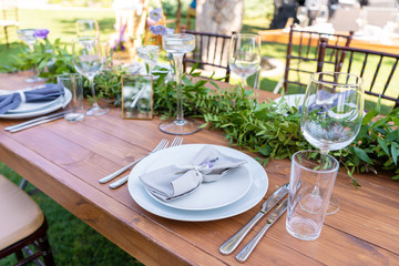 Beautifully decorated wooden table in a summer open-air cafe. Green branch and fresh flowers table decoration.
