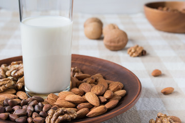 healthy eating concept, almonds, pine nuts, walnuts and a glass of milk on a plate on the table