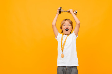 happy boy in a t-shirt with a medal on his neck raises the winner's cup on a yellow background with...