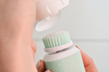 Girl is cleaning face with electric brush. Woman with special brush for deep cleansing facial remove makeup. Skin Care concept. High technology beauty.