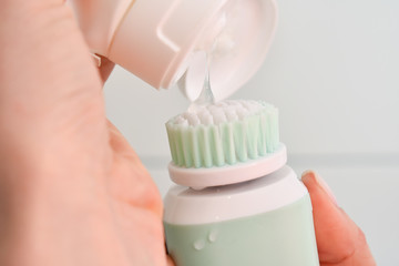 Girl is cleaning face with electric brush. Woman with special brush for deep cleansing facial remove makeup. Skin Care concept. High technology beauty.