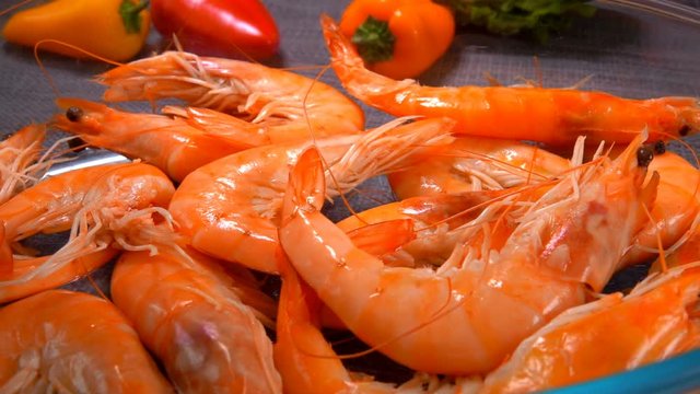 Close up of a delicious unpeeled shrimps in a glass bowl on the background of tomato and pepper