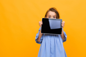 charming attractive caucasian girl in dress shows tablet display on bright yellow background