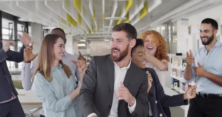 Front view of friendly office team enjoying success in modern office. Multiracial happy office workers funny dancing, moving, smiling, raising hands up. Concept of people, victory, work.