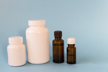 white bottles for pills and glass bottles for essential oils on blue background. Medical, pharmacy and healthcare concept mock up.. Copy space