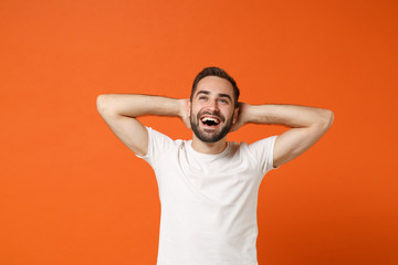 Fototapeta na wymiar Laughing young man in casual white t-shirt posing isolated on orange wall background, studio portrait. People sincere emotions lifestyle concept. Mock up copy space. Looking up with hands behind head.