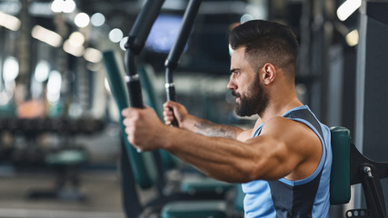 Young bodybuilder exercising on training apparatus at gym