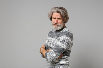 Side view of elderly gray-haired mustache bearded man in knitted sweater posing isolated on grey wall background, studio portrait. People lifestyle concept. Mock up copy space. Holding hands crossed.