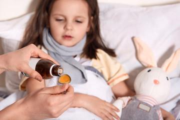 Horizontal photo of unknown hand pouring liquid into spoon from little bottle with syrup, person...