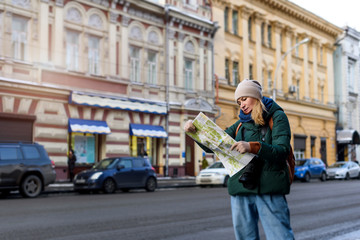 Girl in winter clothes with camera in the historical center of the city is reading a map while...