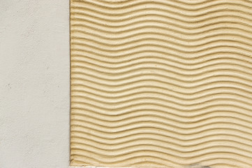 Wellenlinien als Ornament aus Putz auf Außenfassade in Farbe beige auch als Hintergrund nutzbar, mittlere, lange und kurze Brennweite, mit angrenzenden Putz