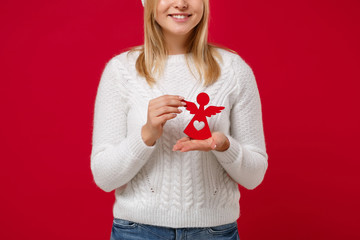 Cropped image of young woman in white sweater, hat isolated on red background in studio. Healthy...