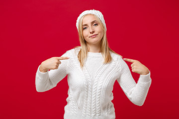 Confident young woman in white sweater hat isolated on red background in studio. Healthy fashion lifestyle people emotions cold season concept. Mock up copy space. Pointing index fingers on herself.
