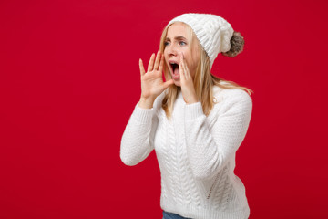 Young woman in white sweater hat isolated on red background studio portrait. Healthy fashion lifestyle people emotions cold season concept. Mock up copy space. Screaming with hands gesture near mouth.