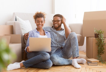 Afro Couple Using Laptop Sitting Among Moving Boxes At Home