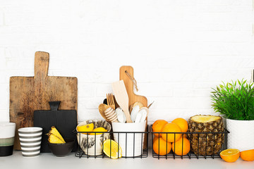 Kitchen shelf storage organization fruit cutlery. Home style minimalism zero waste. Still life with storage baskets of pineapple, oranges, lemons on a white brick background. The modern trend of
