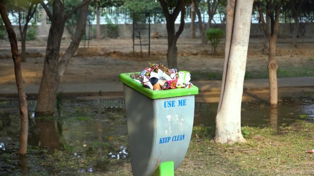 Panning shot from behind plants and trees to a dustbin which is part of the clean india swach bharat program