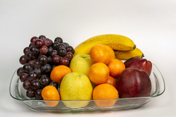 Grapes, red and green apples, tangerines and bananas on a transparent plate. Ripe fruits on a transparent plate. On a white background. Healthy eating
