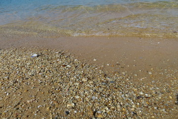 Soft focus of the waves beat at the beach with colorful pebble and shell fragments with sunlight in summer time. Nature background concept.