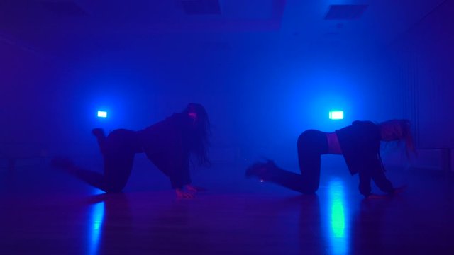 Sexy dance duo in black outfits performing on floor in dark studio