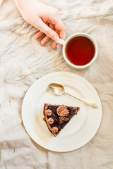 Piece of Dark Chocolate Cake with Chocolate Glaze for Holiday and cup of tea. Top view. Sweet breakfast. Young woman hands. Process of eating