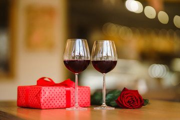 Glasses with wine, rose and red gift box on wooden table. Lovely romantic dinner. Romance at restaurant. Valentines day celebration concept. Relationship, surprise, Birthday concept.