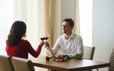 Couple clink glasses with red wine. Lovers give each other gifts. Lovely romantic dinner. Romance at restaurant for Valentine's Day concept. Relationship, surprise, Birthday concept.